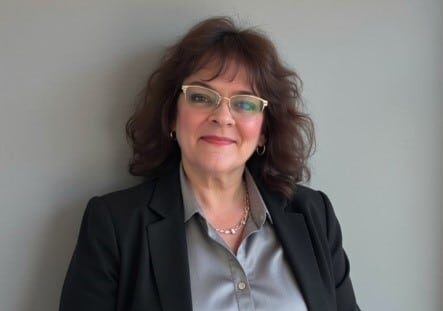 A woman in glasses and blazer smiles into the camera