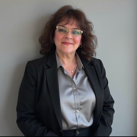 A woman in glasses and blazer smiles into the camera