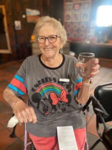 An older woman wearing a Mickey and Mini Mouse shirt holding up a wine glass for cheers